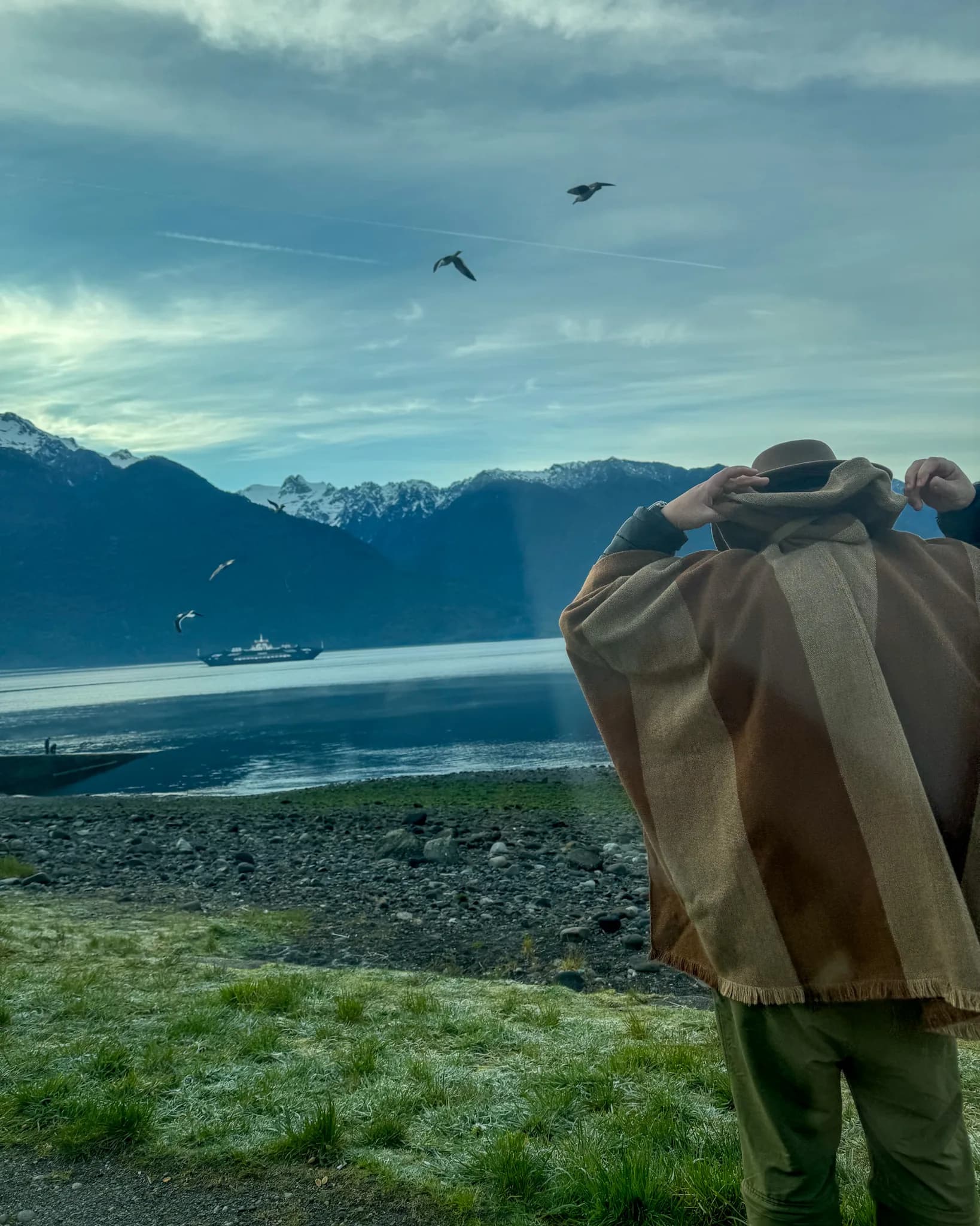 A person in a poncho beside a mountain lake